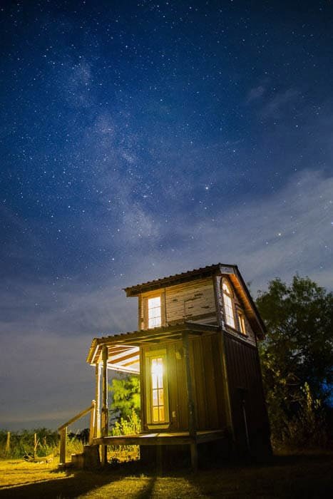 Деревянный домик, снятый ночью на фоне впечатляющего звездного неба