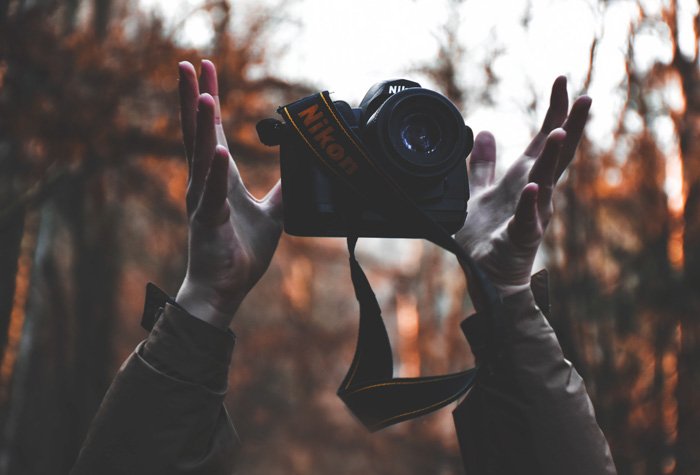 Фотограф игриво подбрасывает в воздух свою камеру Nikon DSLR