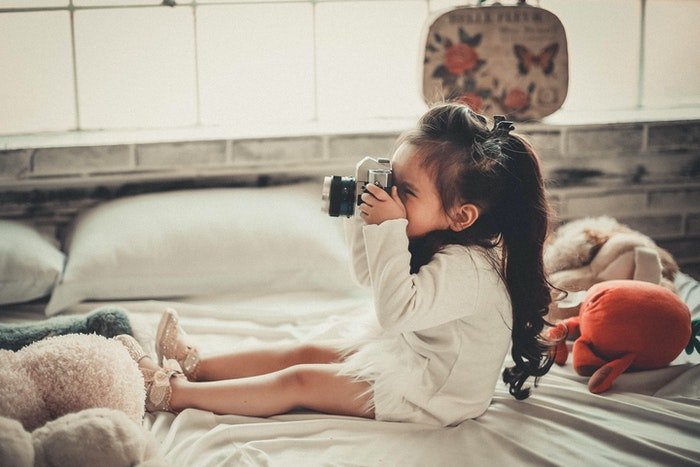 Милая маленькая девочка с фотоаппаратом сидит на кровати