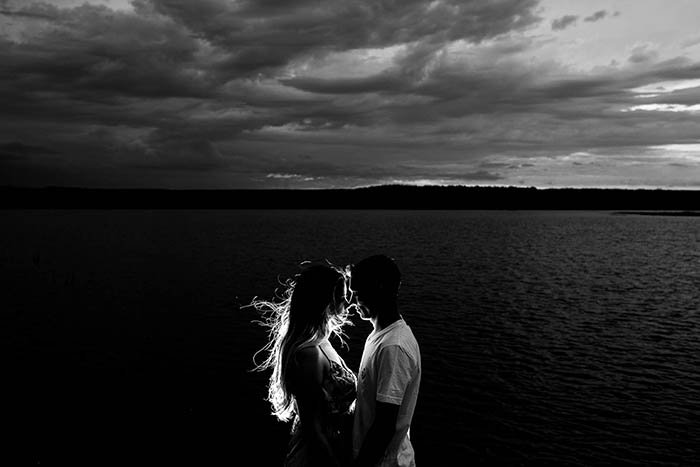 Черно-белая портретная фотография пары с видом на океан на заднем плане. 