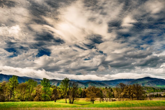 Драматическая погода: Широкое небо с несколькими типами облаков над холмами, полями и лесами