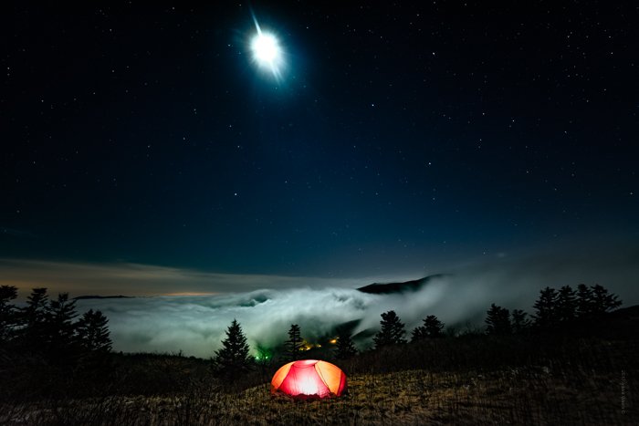 Драматическая погода: Сильный туман, надвигающийся ночью на горизонт, с освещенной палаткой на переднем плане