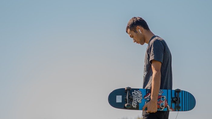 Человек держит скейтборд на фоне голубого неба