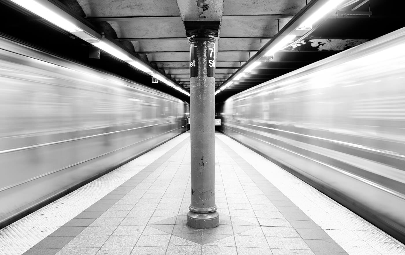 NYC Subway trains rushing by both sides of platform, creating blurred space around the centre