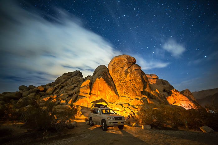 Снимок в Национальном парке Джошуа Три в Калифорнии, на котором изображен белый автомобиль на фоне высоких скал.