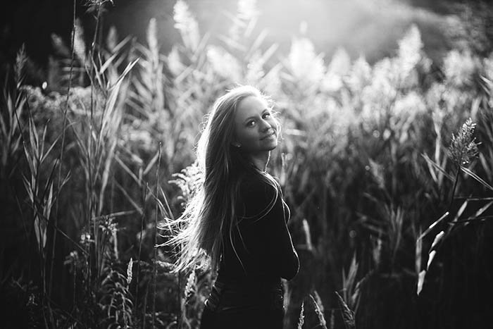 Монохромный портрет молодой женщины в поле, смотрящей через плечо на камеру.
