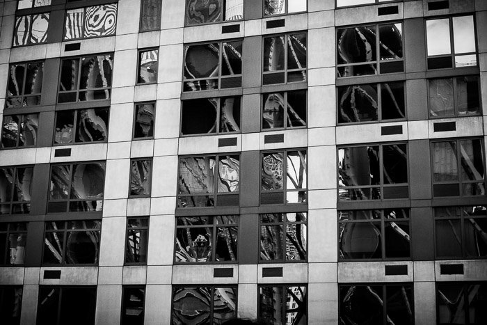 Искаженные отражения в окнах высотного здания. Городская уличная фотография. Монохромные отражения.