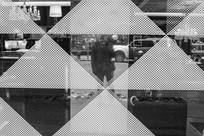 Self portrait taken against patterned window in black and white monochrome