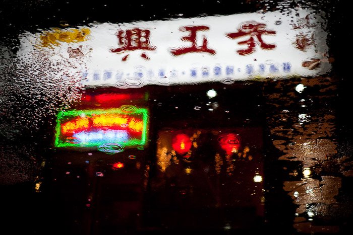 Китайская закусочная с неоновой вывеской, отражающейся в уличных лужах. Городская ночная фотография