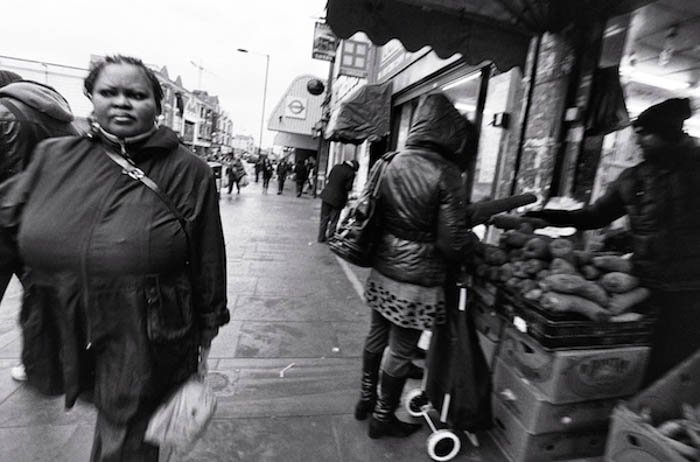 Уличный портрет женщины, идущей по улице, пока другие покупают овощи