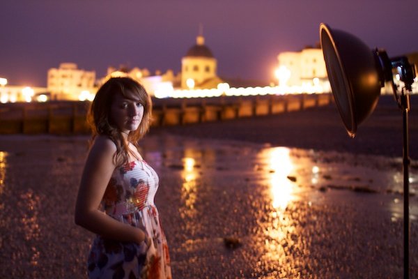Портретная съемка девушки, стоящей на пляже, гавань на заднем плане. Сумеречная фотография.