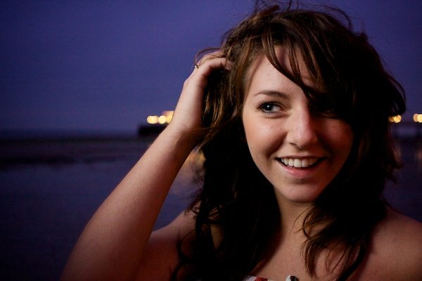Портретная съемка крупным планом девушки с руками в волосах на пляже. Сумеречная фотография.