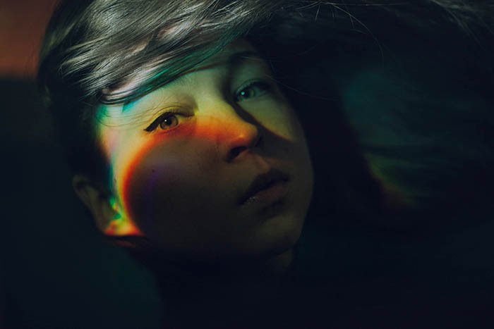 Таинственная автопортретная фотография, показывающая эффект радуги на лице девушки, созданный с помощью компакт-диска