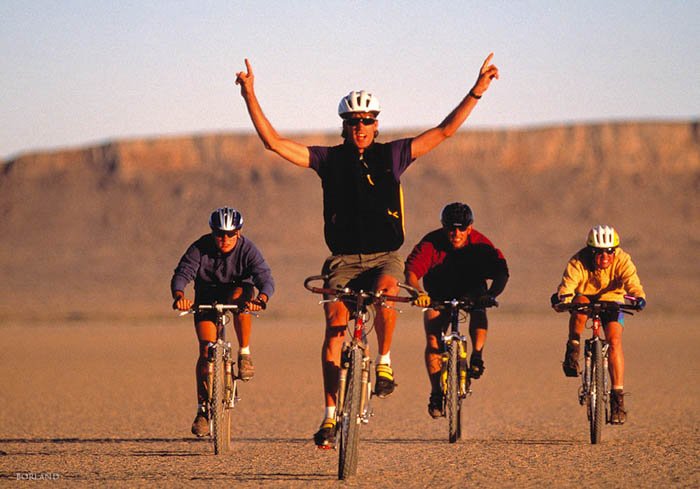 четыре человека едут на велосипедах по пустыне