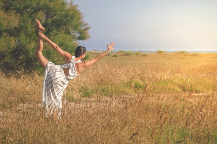 Девушка в белом платье выполняет позу танцовщицы в поле пшеницы