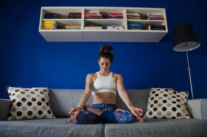 Креативная фотография йоги, показывающая женскую модель в позе лотоса на серой кушетке