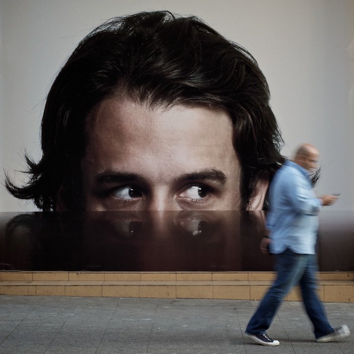 Глаза на рекламе, кажется, следуют за идущим человеком - уличная фотография
