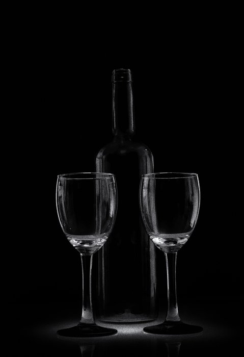 Два бокала и стеклянная бутылка стоят в темной обстановке