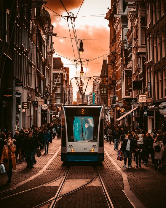 Уличная фотография в оранжевых и голубых тонах с трамваем и толпой людей