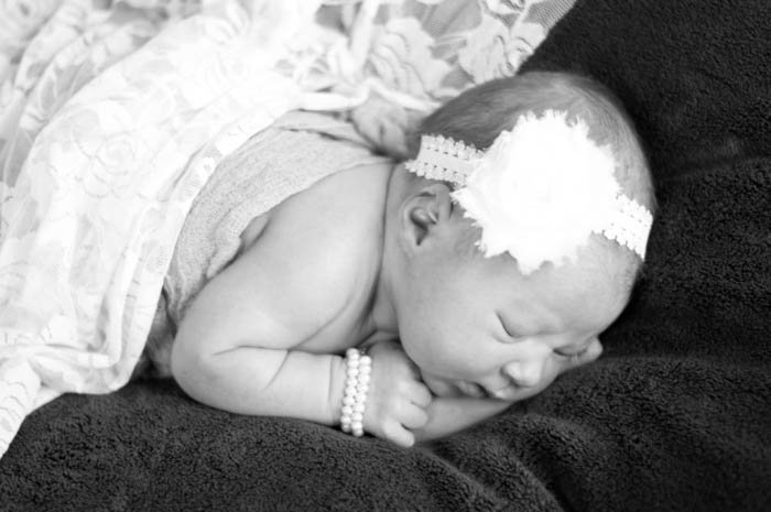 традиционная фотография новорожденного спящего ребенка на одеяле с повязкой на голове и жемчужным браслетом