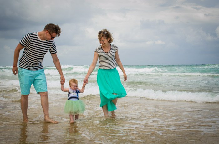 семья из трех человек идет по волнам на пляже