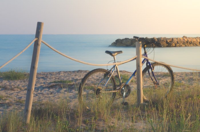 Мечтательная фотография велосипеда, упирающегося в деревянный забор, на фоне моря