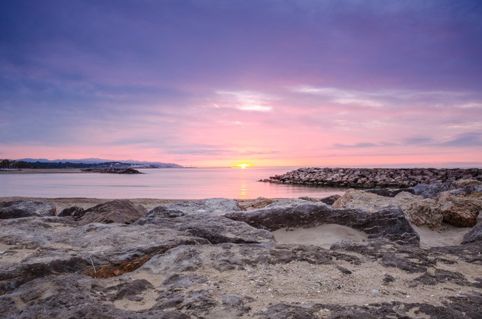 Красивый пляжный пейзаж на закате, со скалами на переднем плане и розовым небом на заднем