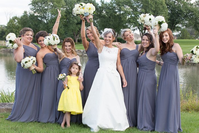 Игривый свадебный снимок, на котором невеста с 7 подружками невесты и 1 цветочницей держат букеты белых цветов в воздухе