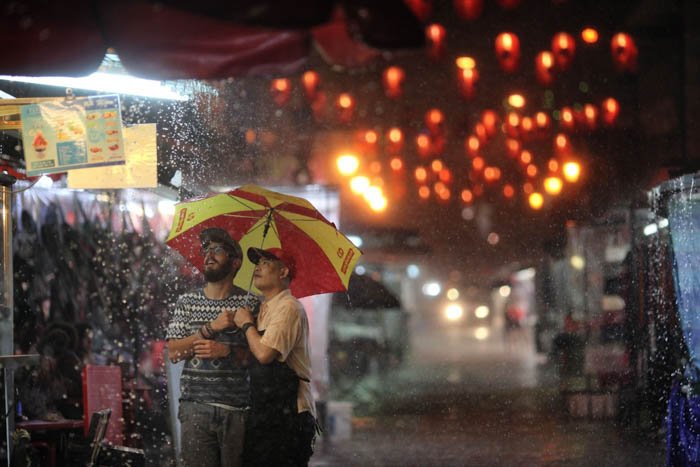 Двое мужчин на дождливом открытом рынке ночью, освещенном разноцветными фонарями