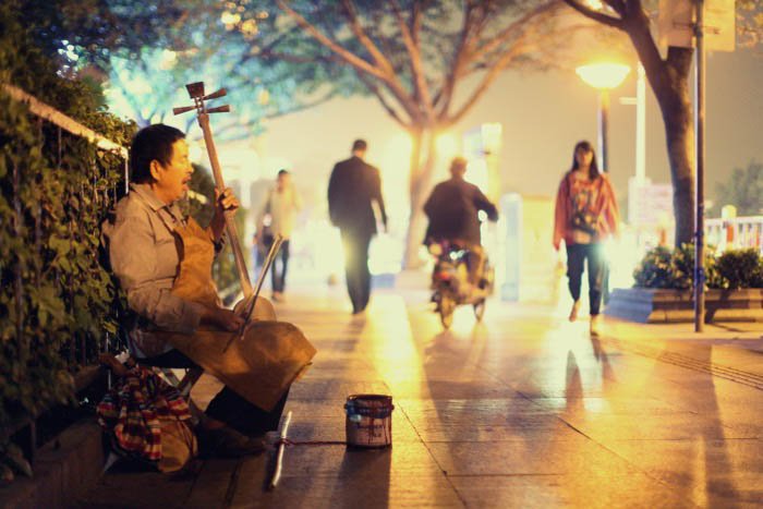 Уличный музыкант играет на струнном инструменте на улице города ночью