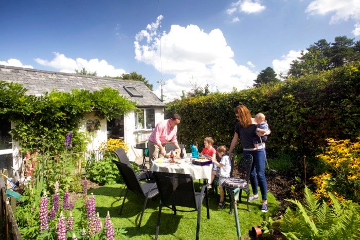Семья обедает на свежем воздухе в маленьком солнечном саду с цветами