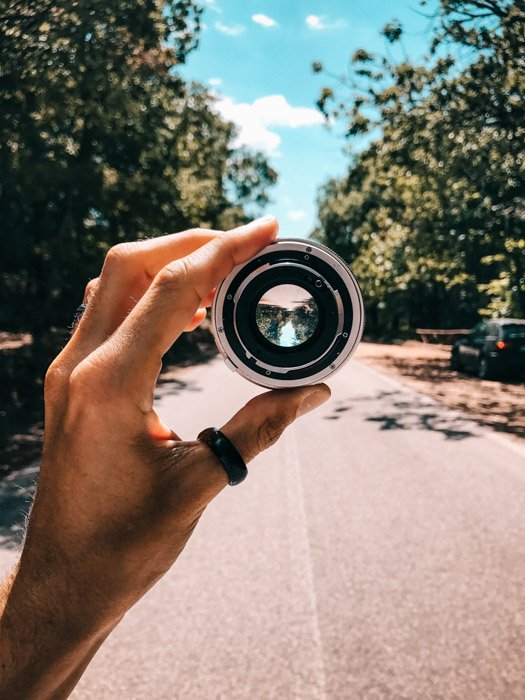 Рука, держащая объектив камеры, показывает городскую дорогу с деревьями по бокам