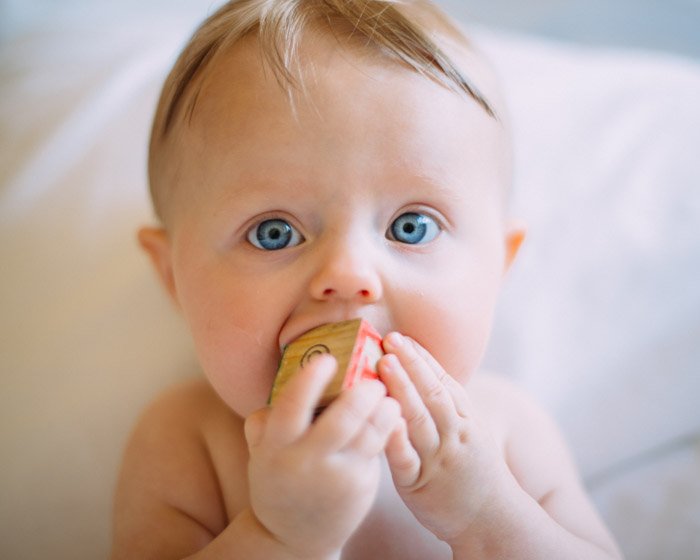 Фотография новорожденного ребенка, грызущего деревянный брусок