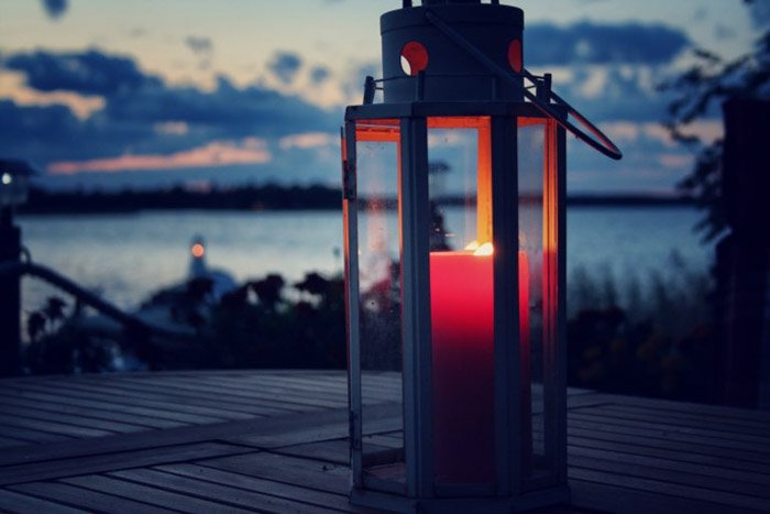 Красная свеча, зажженная в фонаре, установленном на деревянном столе возле озера в сумерках