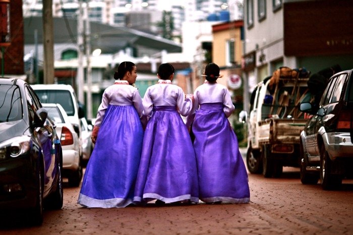 Уличная фотография трех женщин в фиолетовых платьях, идущих по улице. 