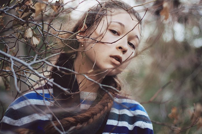 Портрет темноволосой девушки на размытом фоне леса. 