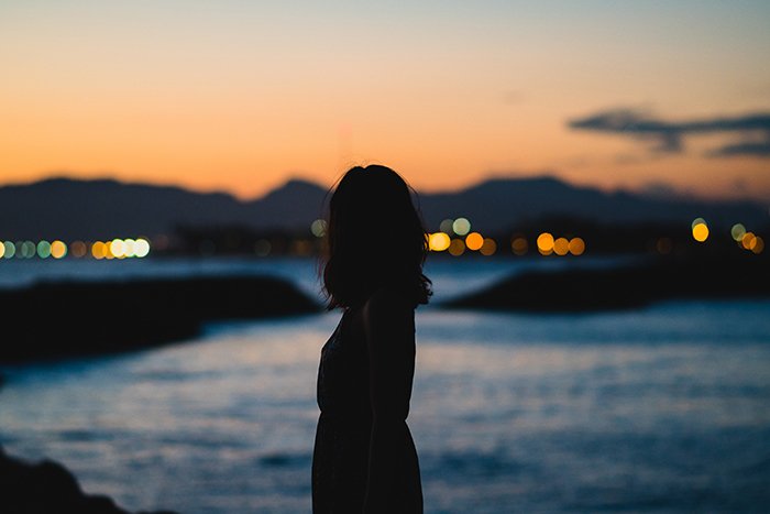 Силуэт женщины, стоящей на переднем плане вечернего морского пейзажа - безликая портретная фотография
