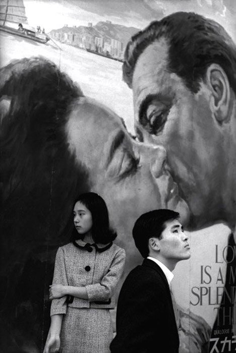 Анри Картье-Брессон фотографирует мужчину и женщину, стоящих на фоне нарисованной целующейся пары.