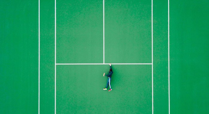 Фотография сверху мужчины на теннисном корте, но выглядит он так, будто держится за выступ
