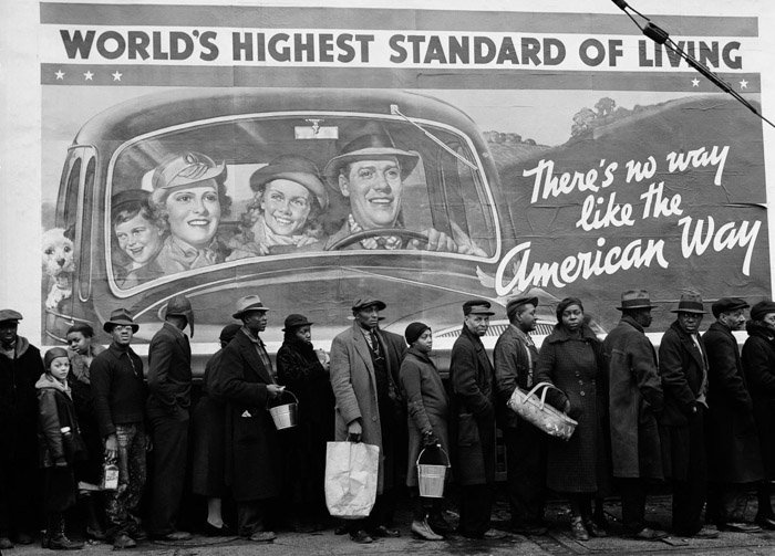 Черно-белая фотография множества людей в очереди за едой на переднем плане в сопоставлении с рекламным щитом с надписью 