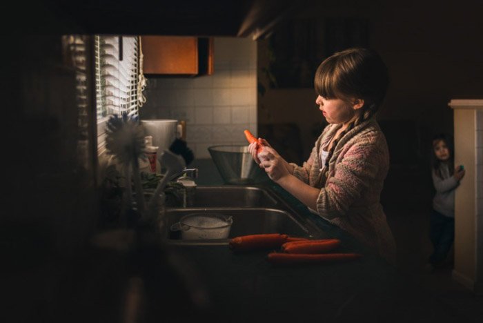Фотография маленькой девочки, чистящей морковь у кухонной раковины