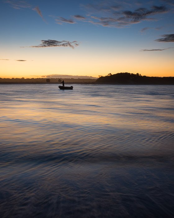 Фигура в маленькой лодке на воде вечером. Композиция пейзажной фотографии