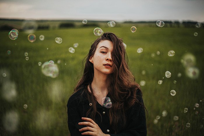 Портрет девушки в естественном свете, стоящей на зеленых полях в окружении пузырьков