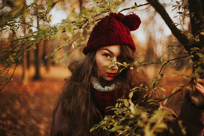 портрет девушки в красной шапочке, смотрящей сквозь деревья в прекрасный осенний день - портреты в естественном свете