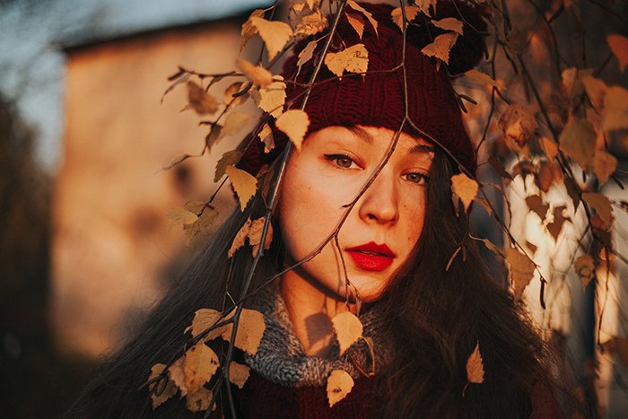 портрет девушки в красной шапочке в естественном свете, смотрящей на осенние деревья