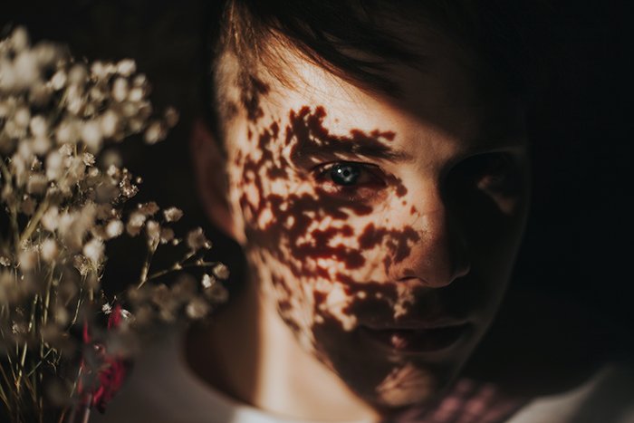 Теневой крупный план лица девушки, букет цветов отбрасывает мечтательные тени на ее лицо. Портретная съемка при естественном свете