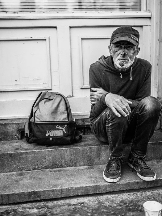 Черно-белая уличная фотография бездомного, сидящего на ступеньке в Будапеште, сделанная на камеру Panasonic gh5 Крейгом Халлом