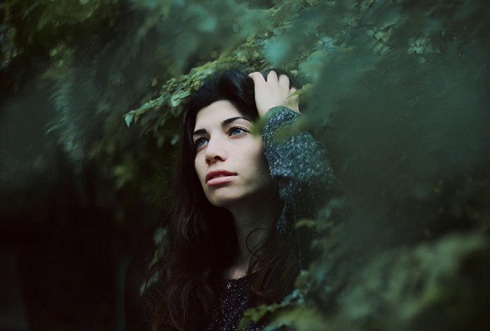 Таинственный портрет темноволосой девушки на размытом фоне леса. 