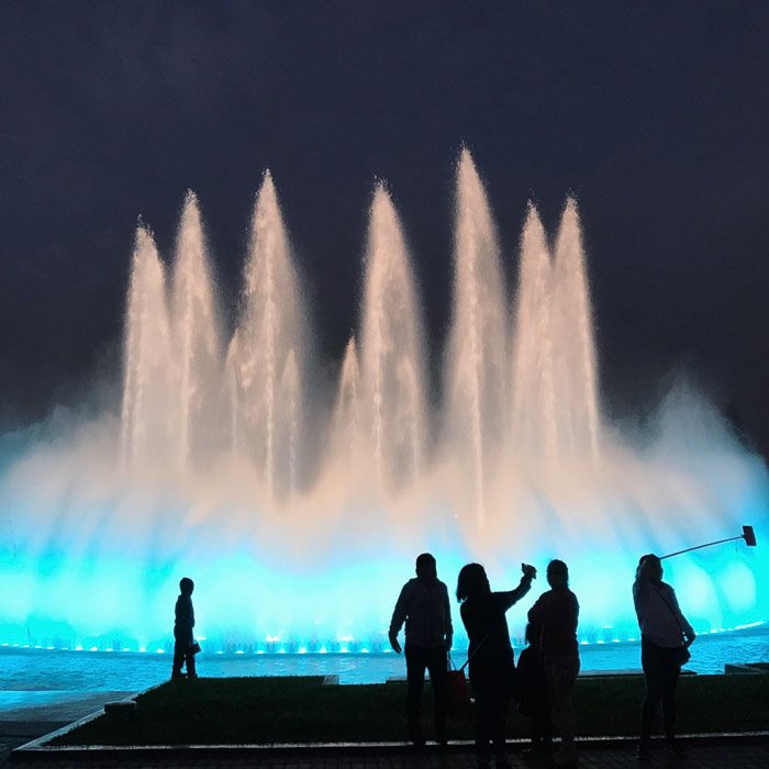 Фотография красивого фонтана ночью при слабом освещении с силуэтами людей на переднем плане