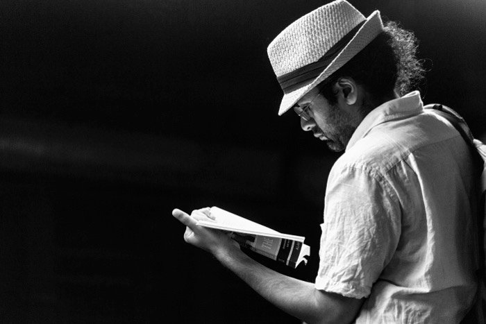 Черно-белая откровенная фотография мужчины в белой шляпе и рубашке, читающего книгу
